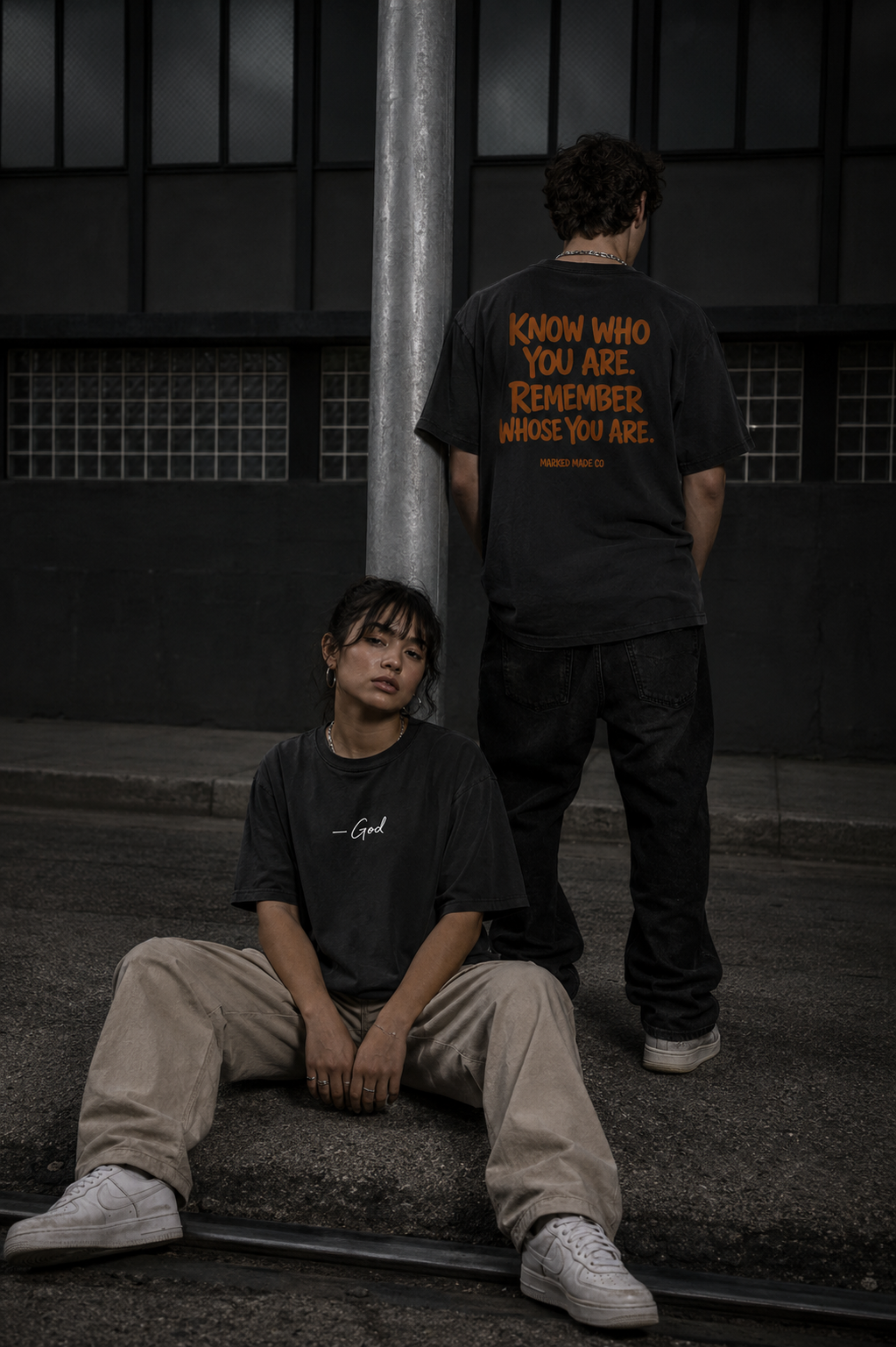 Two people wearing black t-shirts with text, sitting on steps in a dark setting.