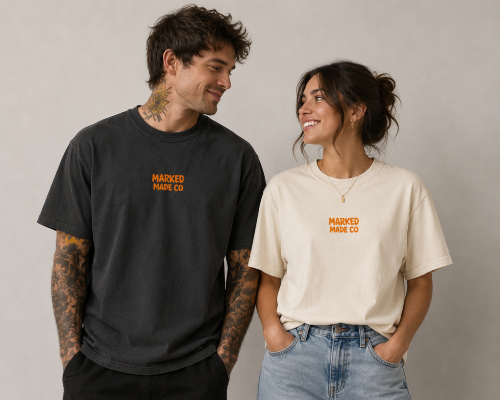 Two people wearing 'Marked Made Co' t-shirts standing against a plain background